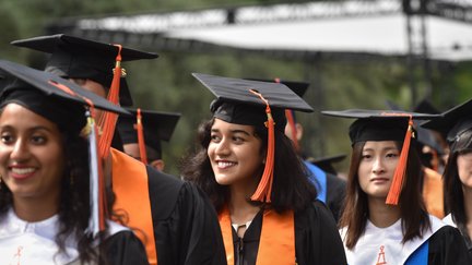 Students are wearing Commencement regarlia and are walking behind one another