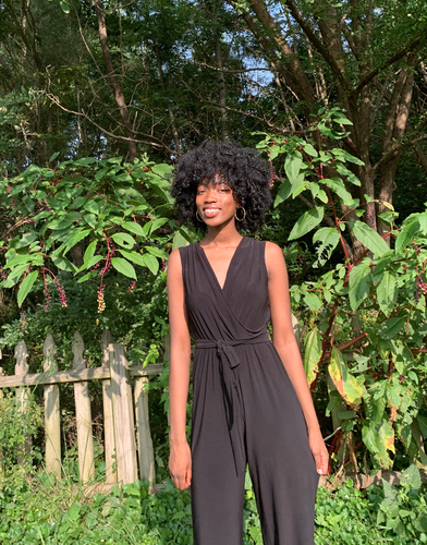 Ayooluwa smiling and standing in front of a fence and lush greenery.