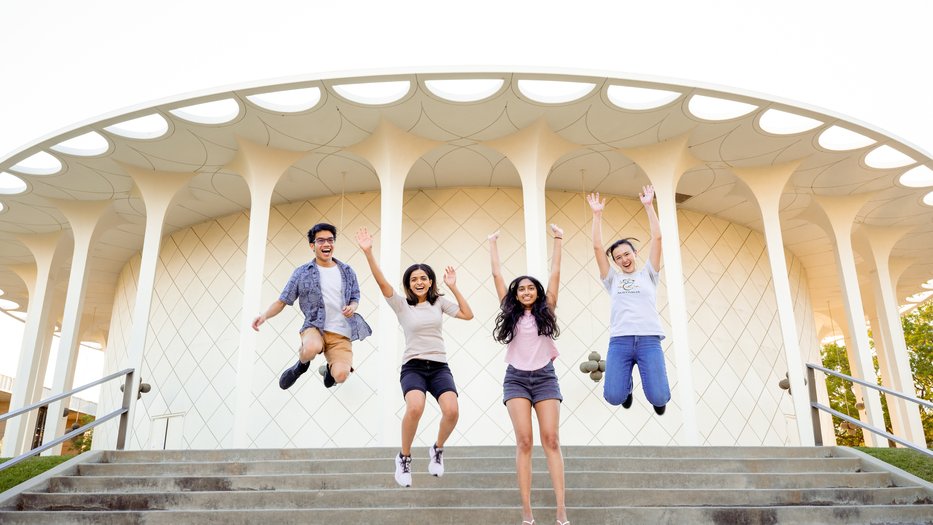 Four students jumping in front of the Beckman Auditorium stairs.