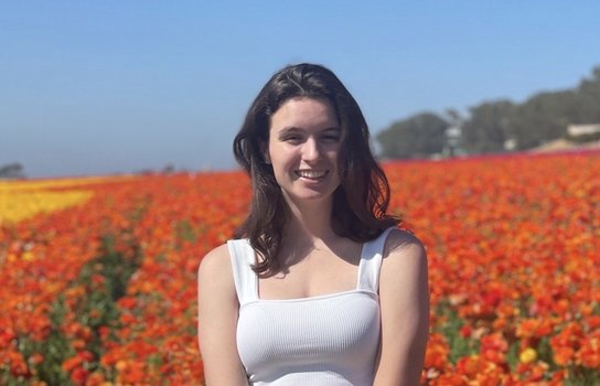 Profile photo of Isabel standing in front of a field of flowers on a cloud-free day