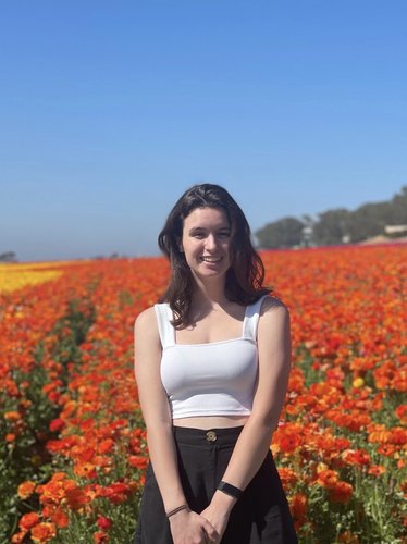 Profile photo of Isabel standing in front of a field of flowers on a cloud-free day