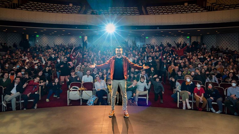 YouTuber Mark Rober in Caltech's Beckman Auditorium with an audience abd backlight behind him