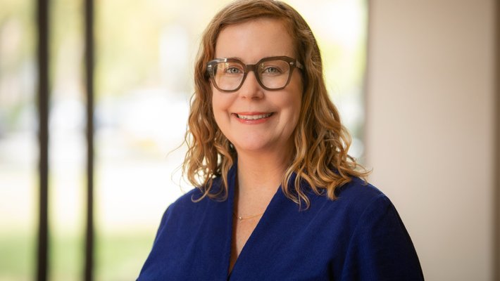 headshot of Susanne Hall - dark blond hair, navy shirt, glasses