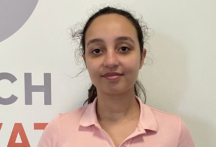 A young woman in a pink shirt standing in front of a logo