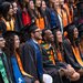 A group of smiling students wearing graduation robes and caps with many different colored sashes