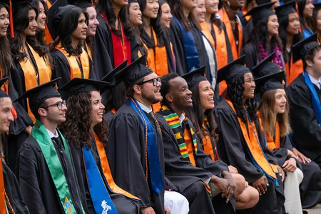 A group of smiling students wearing graduation robes and caps with many different colored sashes