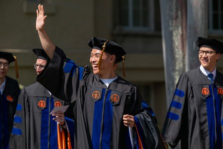 Three Caltech graduates enter their commencement ceremony. One is waving to someone outside the photo's frame.