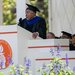 An older man wearing graduation robes with a blue stole speaks to an audience from a lecturn