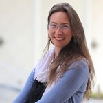 Franca Hoffmann, with long light brown hair and glasses, wearing a white scarf and a light blue sweater, stands outside Beckman Auditorium on the Caltech campus.