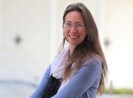 Franca Hoffmann, with long light brown hair and glasses, wearing a white scarf and a light blue sweater, stands outside Beckman Auditorium on the Caltech campus.