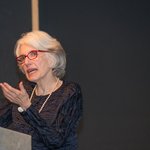 An image of Dava Sobel speaking behind a podium.