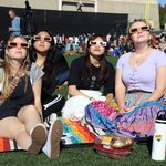 Four teenage girls wearing eclipse glasses on athletic field