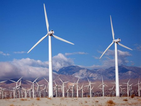 Wind turbines spin in front of a backdrop of clouds and mountains.