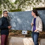 two people in discussion in front of an outdoor chalkboard