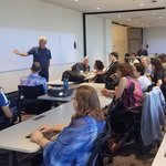 students in classroom with professor at whiteboard