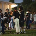 People gather around a telescope on a lawn with Beckman Auditorium in the background