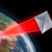 An artist's rendering showing a gray or silver square sail being pushed through space by a red laser beam. Earth is in the background.