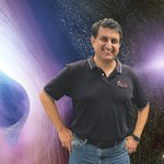 Varoujan Gorjian standing in front of an artist's rendering of the gaseous accretion disk of an active galactic nucleus