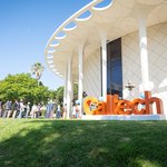 Students walk into the Beckman Auditorium. In the foreground are large orange letters spelling out 