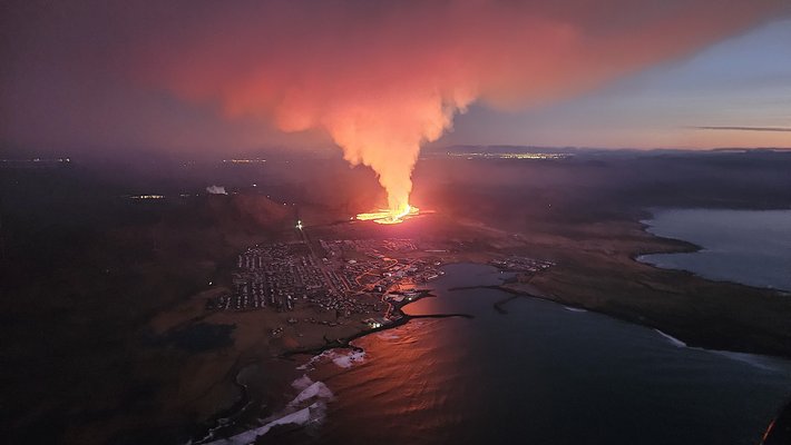 A red plume of lava near a town on a coastline
