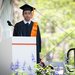 A young man wearing a black robe and mortarboard with an orange tassle stands as a commendation for him is read out.