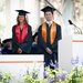 Two college graduates, both in graduation garb stand side by side. One is a young woman with a red sash and medium brown hair and the other is a young man with a lavender tie and short black hair.