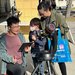 Three people gather behind a telescope on a sunny day