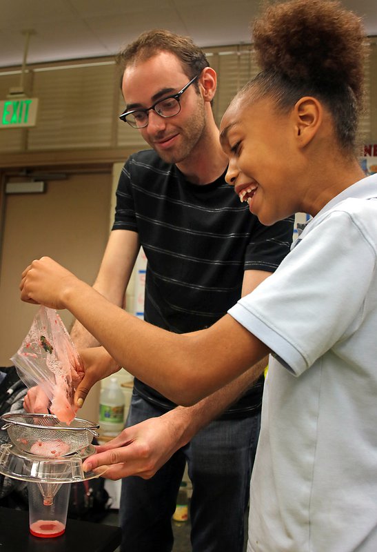 Caltech graduate student Michael Mazza helps a fourth-grade student strain strawberry pulp to extract its DNA.