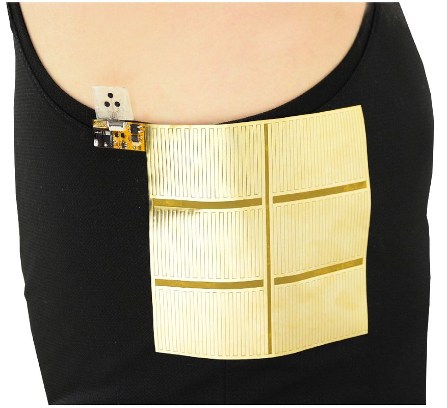 A gold-colored sheet with stripes is attached to the torso of a person wearing a black tank top. A small electronic device is also attached.