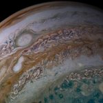 Two white oval storms merge in an orange band on Jupiter