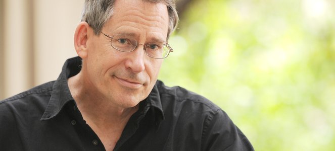 Professor John Preskill, a middle-aged white man, wears wire-rimmed glasses and a black shirt.