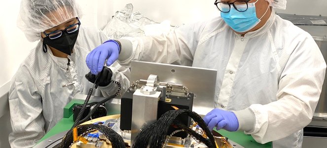 Scientists working on an instrument in lab, wearing protective suits.