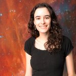 Sandra O'Neill wearing a black shirt and jeans, standing in front of an image of outer space