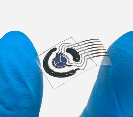 A close-up photo of a flexible sweat sensor being held between two gloved fingers.