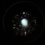 A cluster of stars as seen through a telescope's eyepiece, with a glowing green blob in the middle