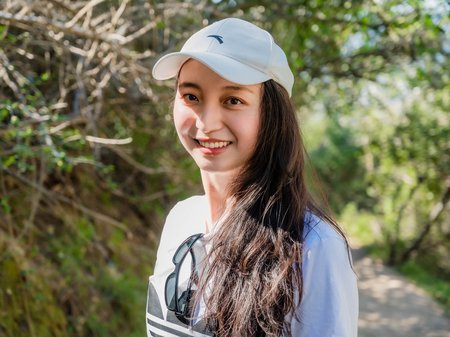 A person with long brown hair and a baseball cap smiles for a photo