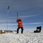 Zhongwen Zhan in a bright red winter coat swinging a sledgehammer at the Antarctic ice