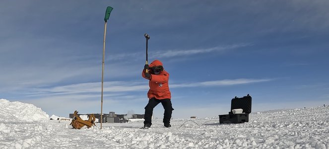 Zhongwen Zhan in a bright red winter coat swinging a sledgehammer at the Antarctic ice