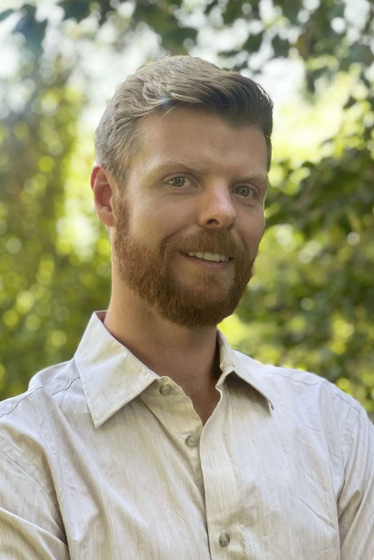 A portrait of Christopher Kenseth. He is outdoors with trees in the background.